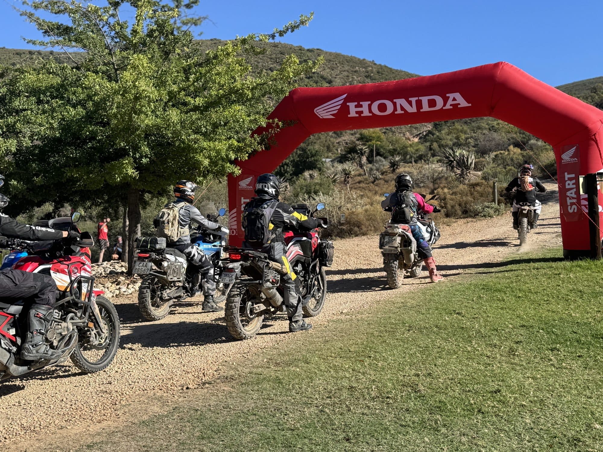 Riders passing under a red Honda inflatable arch on an adventure ride